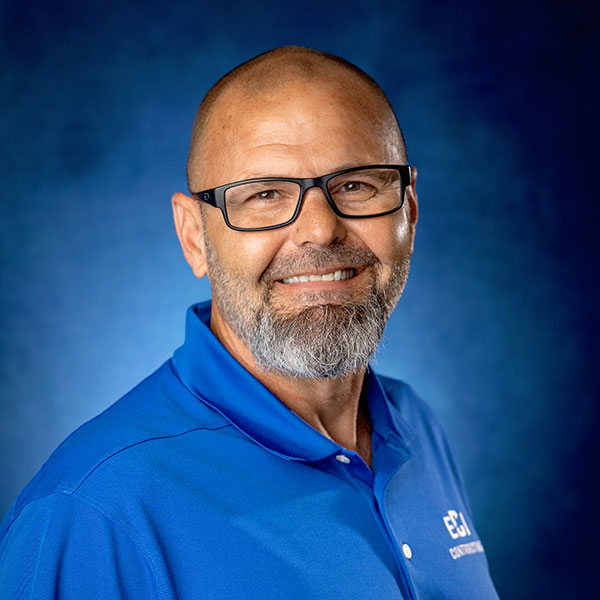 Mike Schibursky, Senior Project Manager at ECI Contracting, smiling in a blue polo shirt with ECI logo, against a blue background.