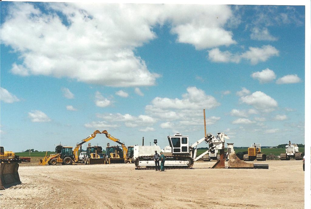 Construction equipment and machinery in a gravel lot, showcasing ECI Contracting's underground construction capabilities, with workers present and a clear blue sky.