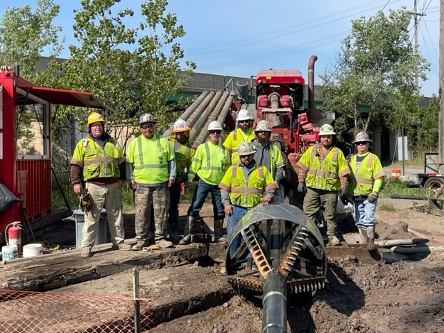 Team of ECI Contracting workers in safety gear posing at an underground construction site, featuring drilling equipment and utility pipes, showcasing expertise in trenchless construction solutions.