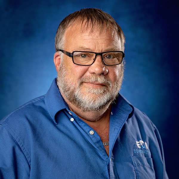 Kurt Peterson, Operations Manager at ECI Contracting, wearing a blue shirt with the ECI logo, against a blue background, reflecting the company's commitment to quality and safety in underground construction.