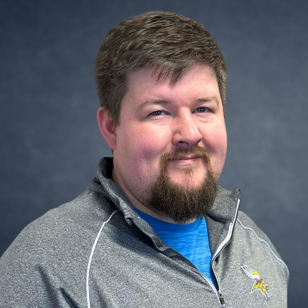 Troy Tumbleson, estimator at ECI Contracting, smiling in a gray athletic shirt against a dark background, representing the company's commitment to quality and safety in underground construction.